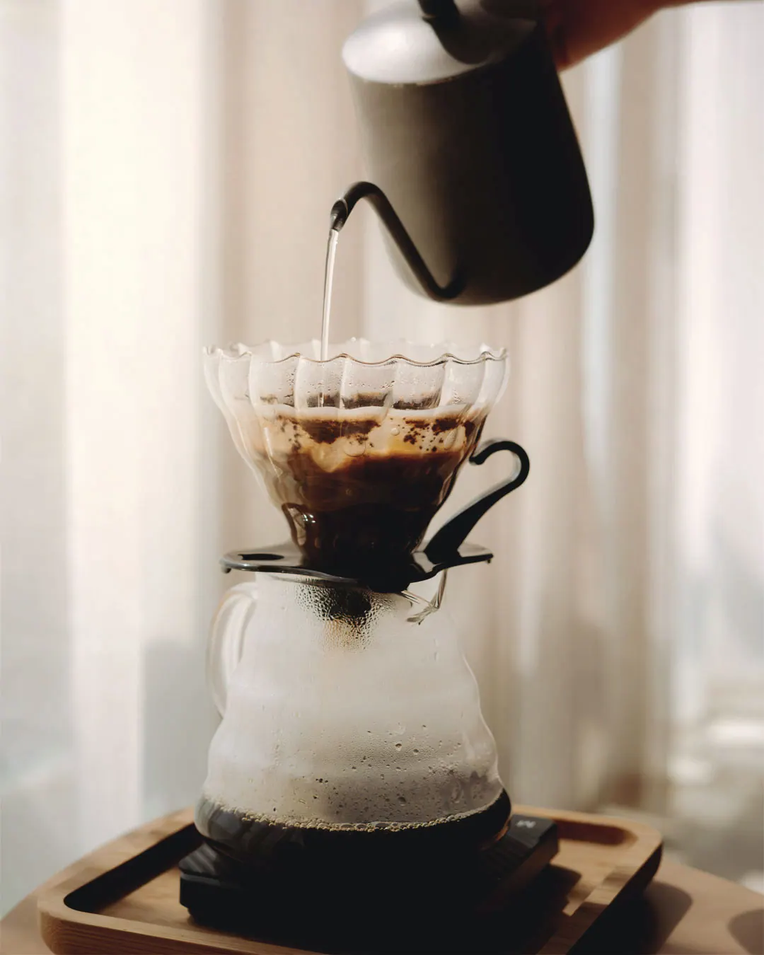 A black kettle pours water into a glass pour-over dripper above a coffee carafe.