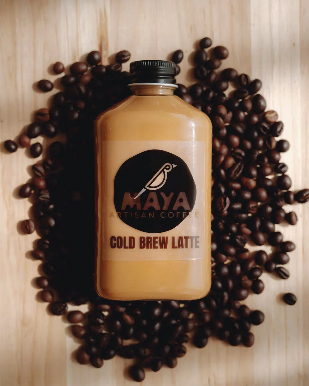 A bottle of Maya cold brew latte lying on a bed of roasted coffee beans.